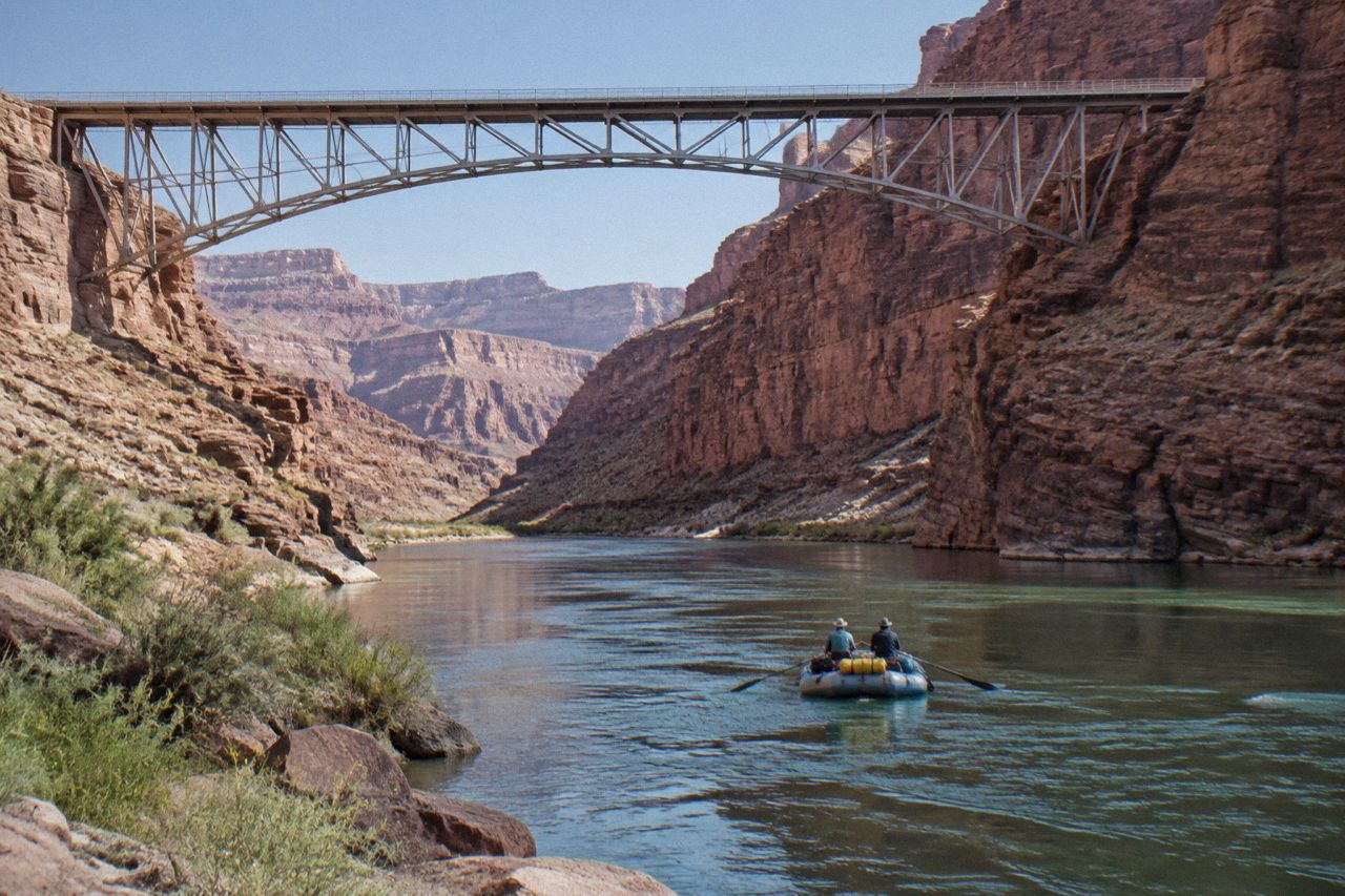 Inflatable raft carrying a small group down the Colorado River between tall canyon walls, seen from river level