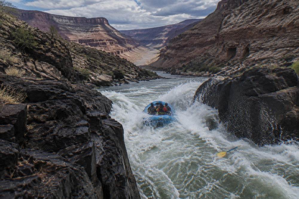 Whitewater raft cutting through a standing wave in a narrow canyon passage