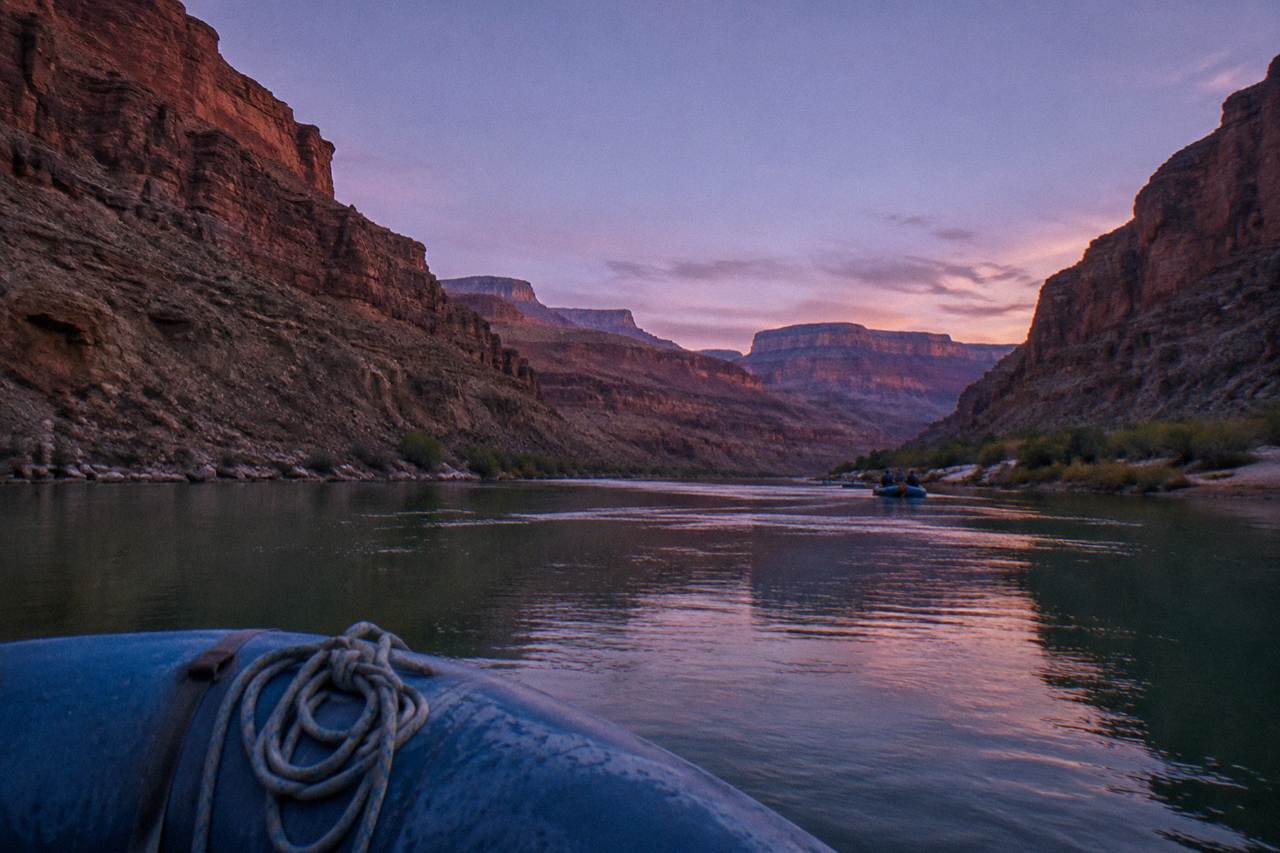 Raft floating on calm green water between tall canyon walls under a wide sky