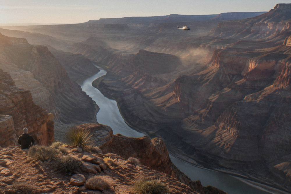 A helicopter flying above layered canyon walls above a winding river