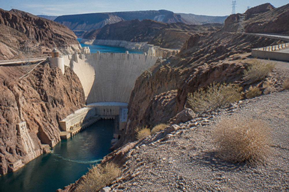 Wide view of a concrete arch dam between rocky desert cliffs under open sky