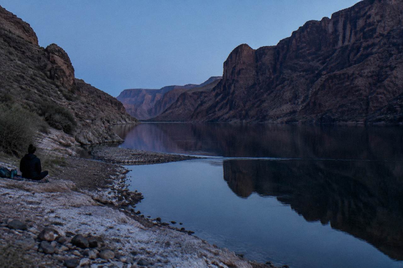 Still water in a desert canyon reflecting tall rock walls under a clear sky
