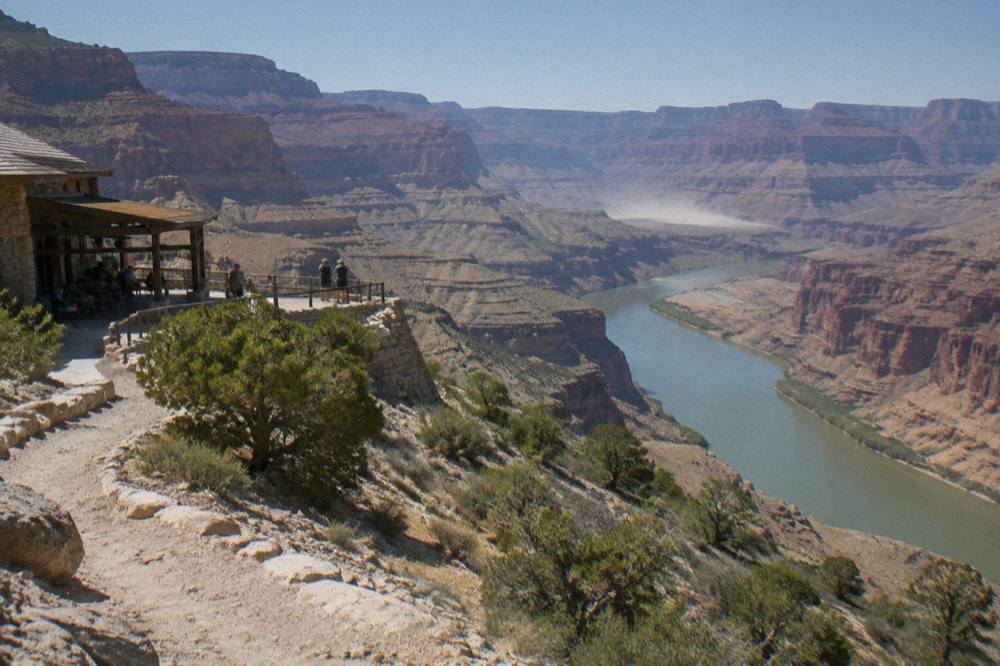 A wide calm stretch of the Colorado River winding between layered canyon cliffs under a clear sky