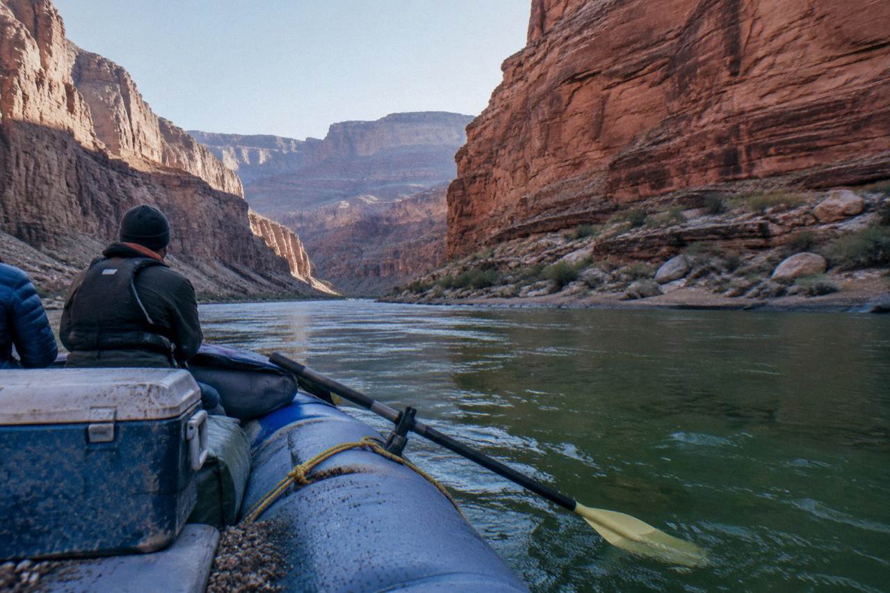 A motorized raft drifting between tall red canyon walls on the Colorado River