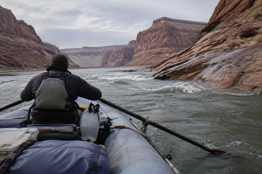 A guide steering an oar raft toward a gentle wave on a wide desert river