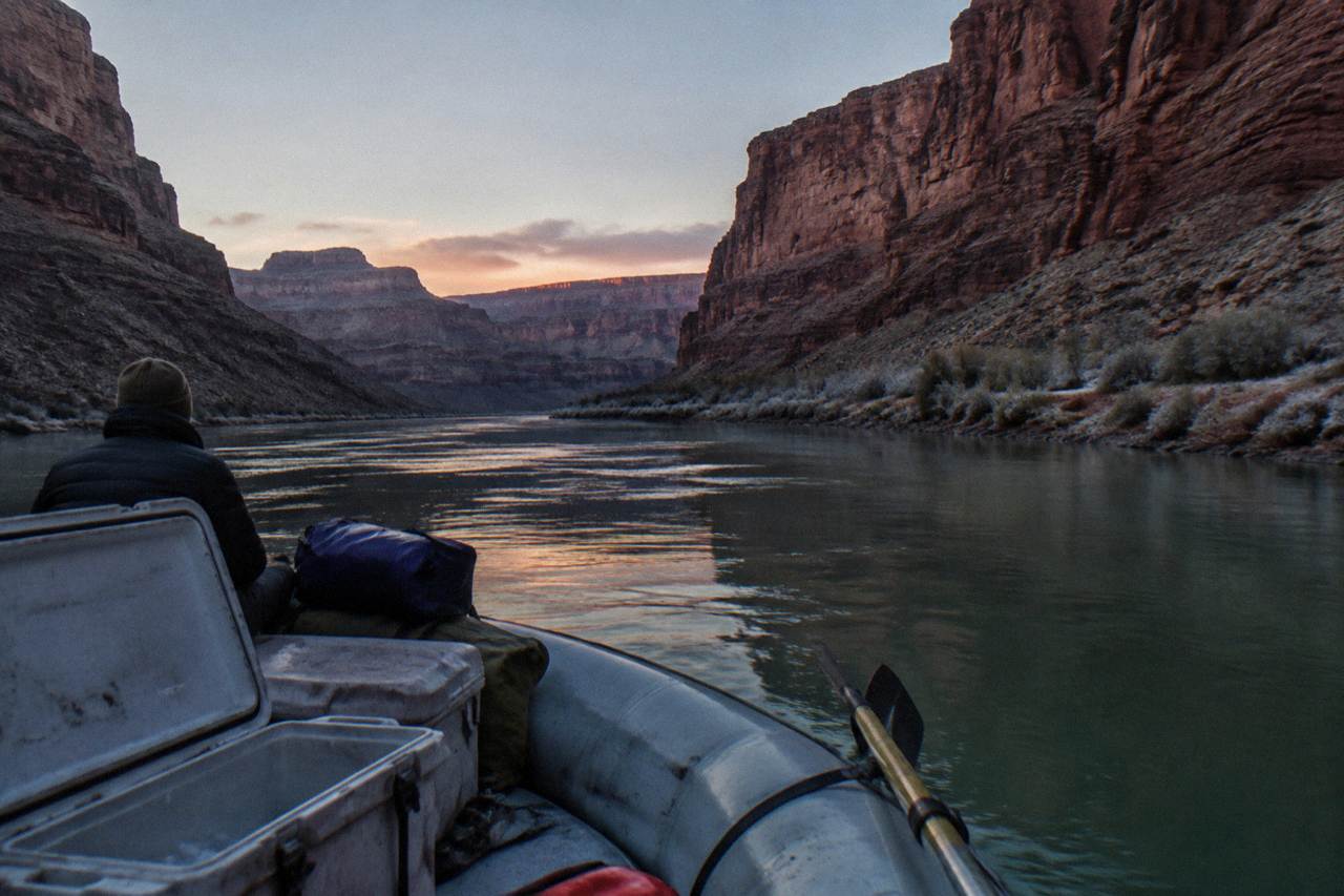 A motorized raft drifting on calm green water between tall canyon walls