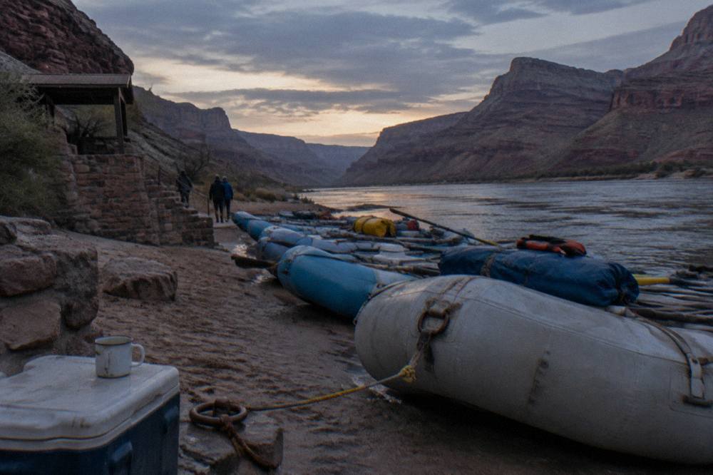 A row of loaded rafts tied up on a sand beach beside the river at dusk