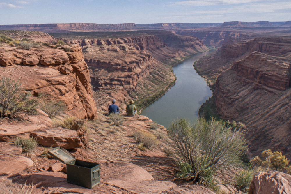A raft crew scouting a calm stretch of river beneath tall red canyon walls