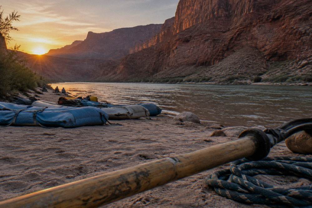 A wide view of rafts resting on a river beach inside a deep canyon at sunset