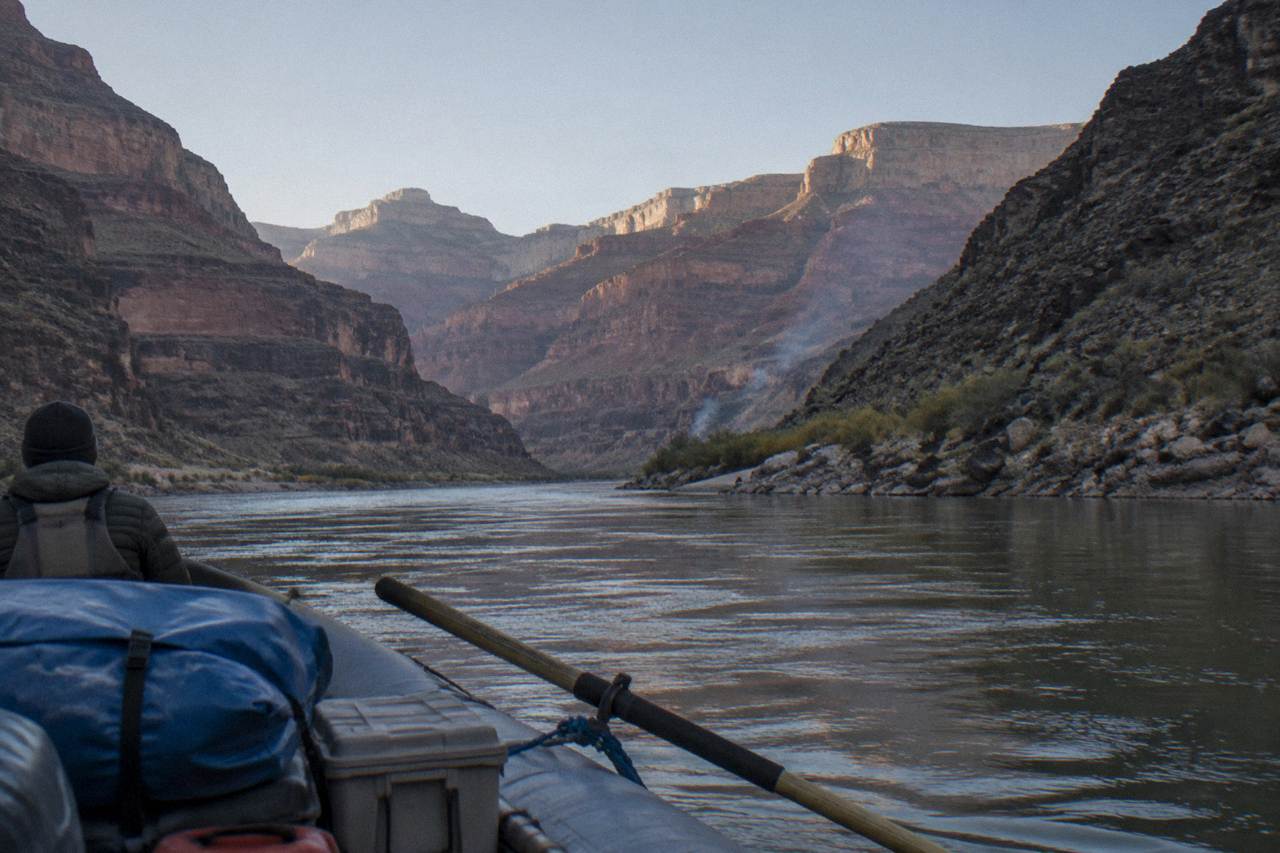 A motorized raft drifting on the calm Colorado River between steep canyon walls