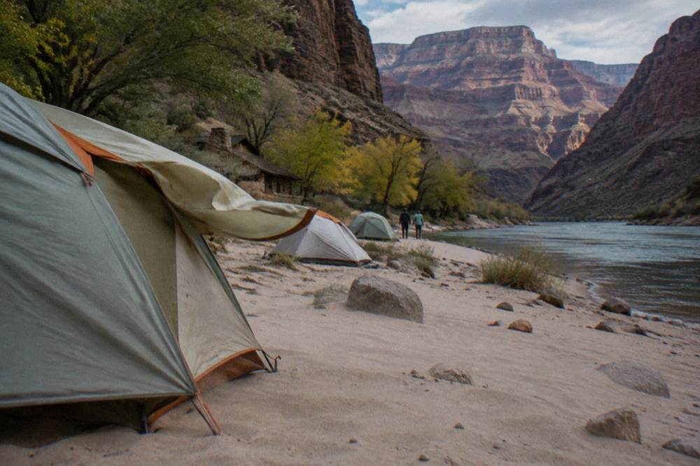 Tents pitched on a sandbar beside the river with canyon walls rising in the background