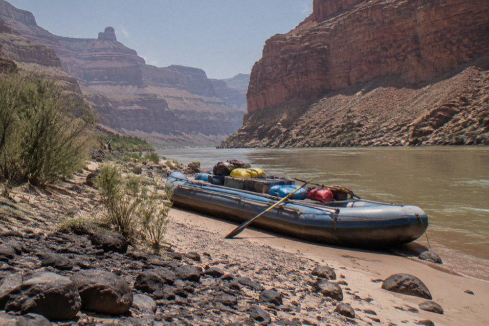 Long motorized raft loaded with gear beachet at a sandy camp below layered canyon walls