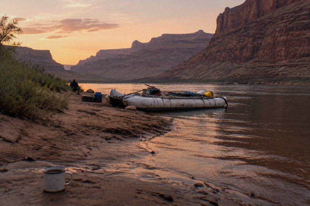 Camped raft on a sand beach at dusk with canyon walls rising on both sides