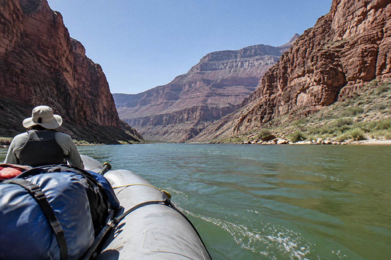 Motorized raft drifting between tall red canyon walls above the Colorado River