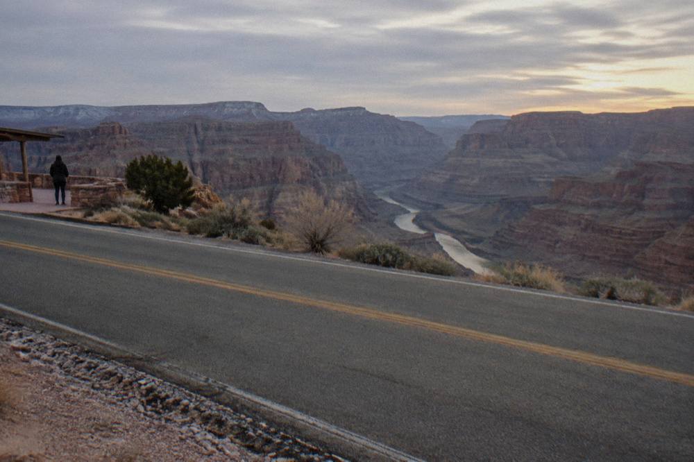 An empty two-lane road crossing open scrubland toward distant canyon cliffs