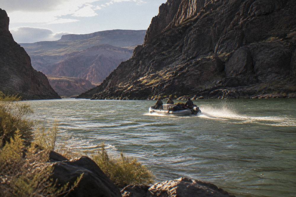 A motorized raft on a wide stretch of the Colorado River between dark canyon walls
