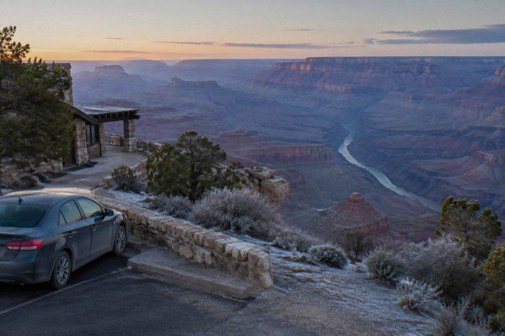 A parked car at a canyon overlook with layered rock formations stretching to the horizon