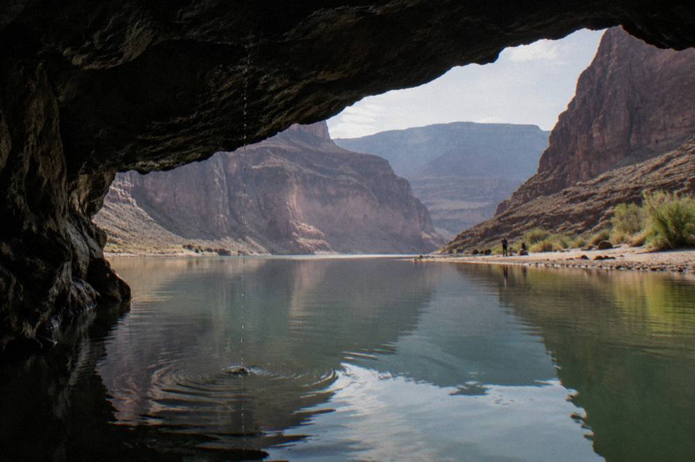 A green-tinted river cave opening reflecting still water between dark rock walls