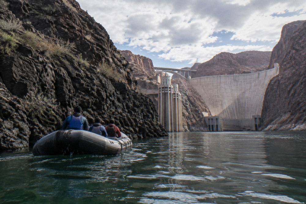 A motorized raft drifting along a dark canyon wall above still green river water