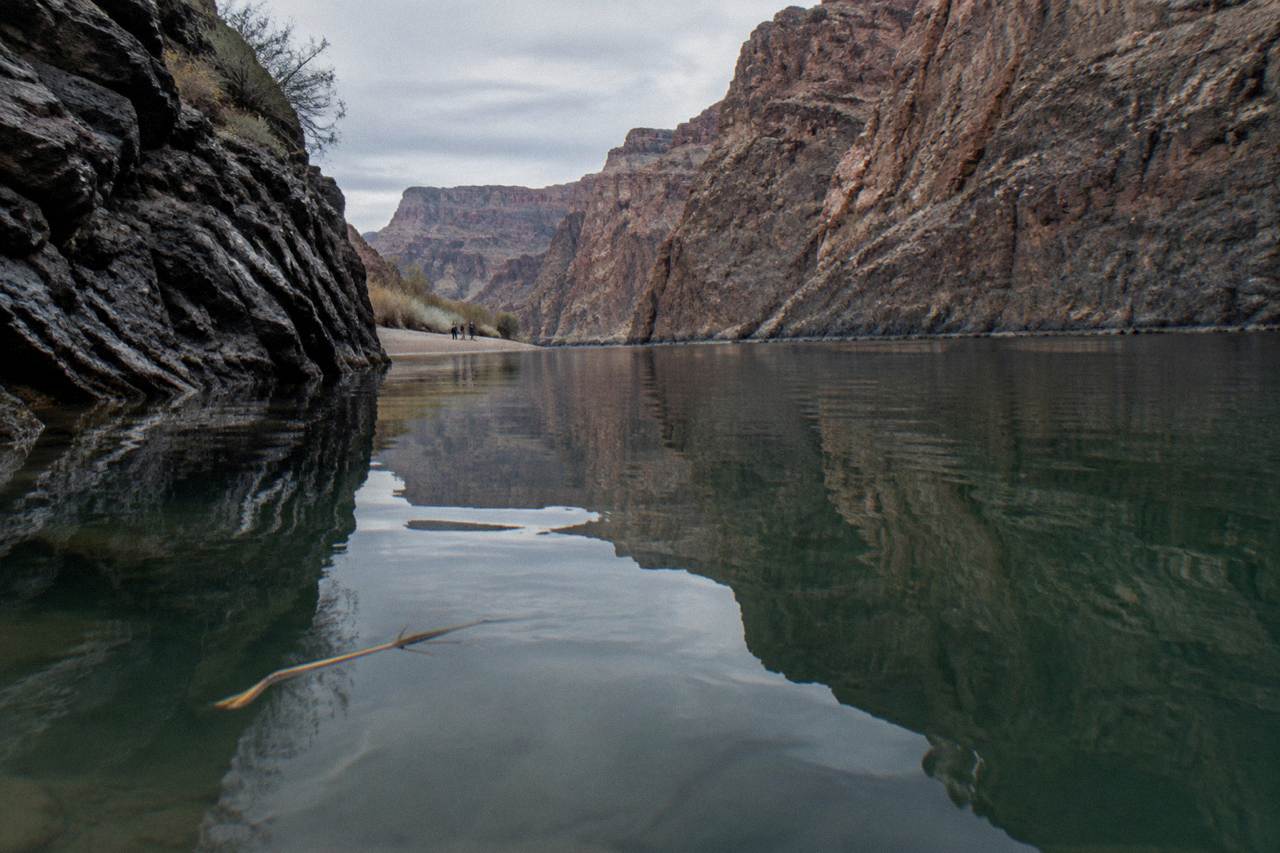 Calm green river water reflecting canyon walls inside a dim desert canyon