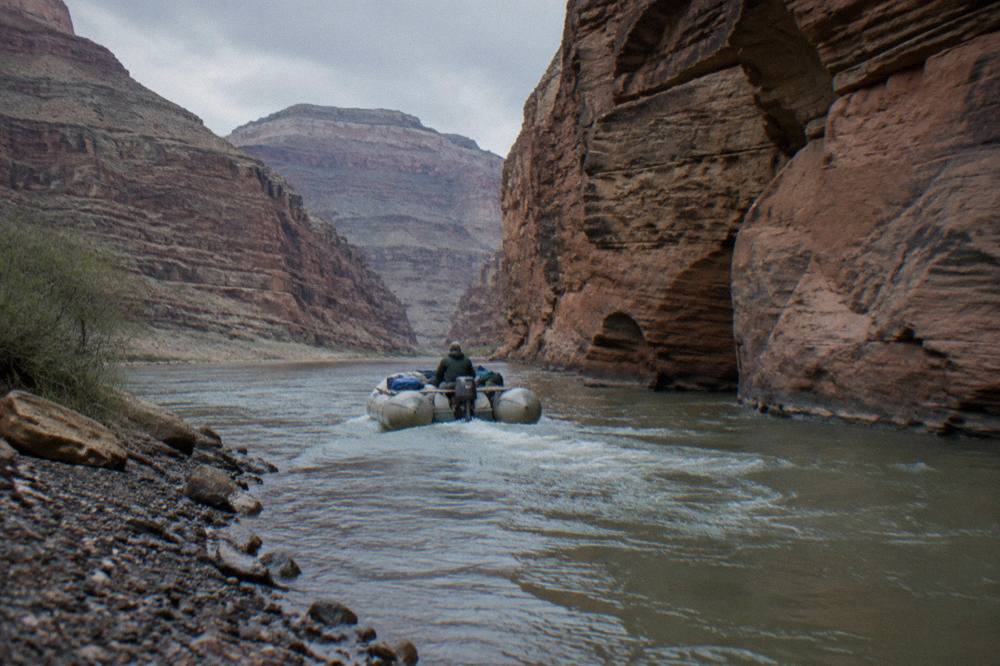 A motorized raft carrying passengers through a narrow canyon passage on the Colorado River