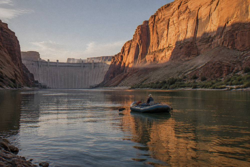 A motorized raft drifting on calm green water beneath steep canyon cliffs