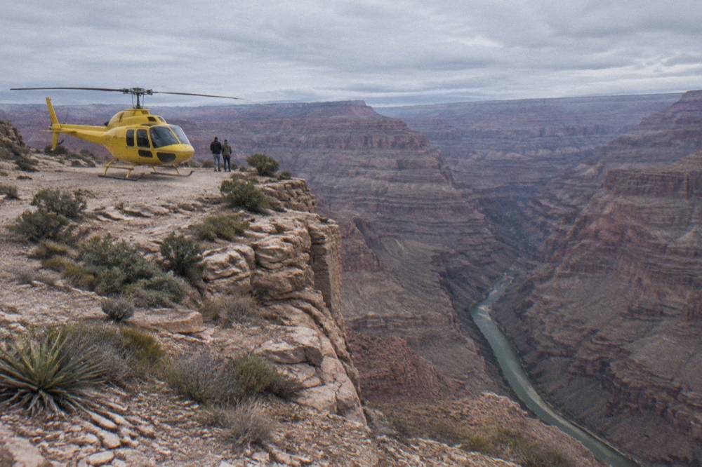 A yellow helicopter parked on a rocky ledge above a narrow river gorge