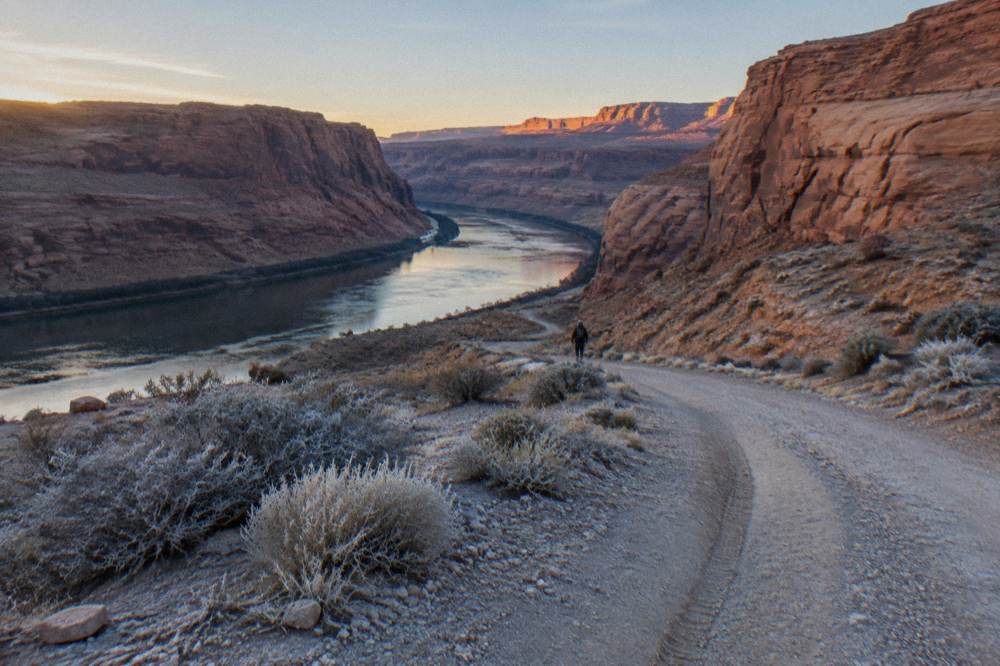 An empty gravel road winding toward a river corridor at dawn