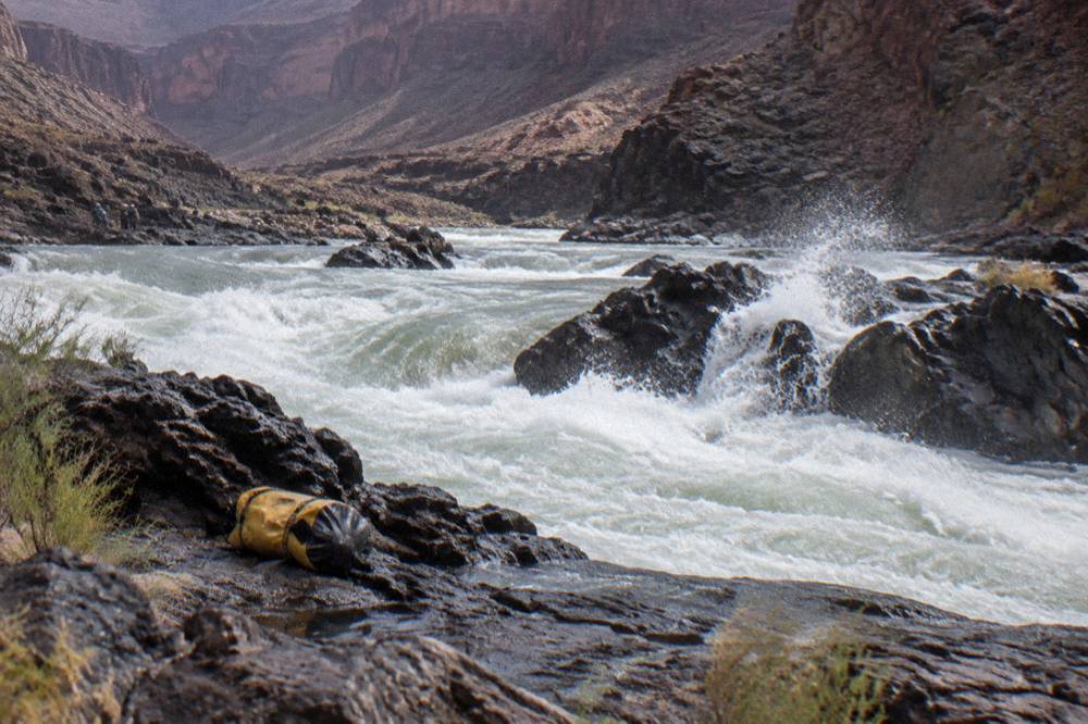 Turbulent whitewater waves curling around rocks in a narrow canyon river channel