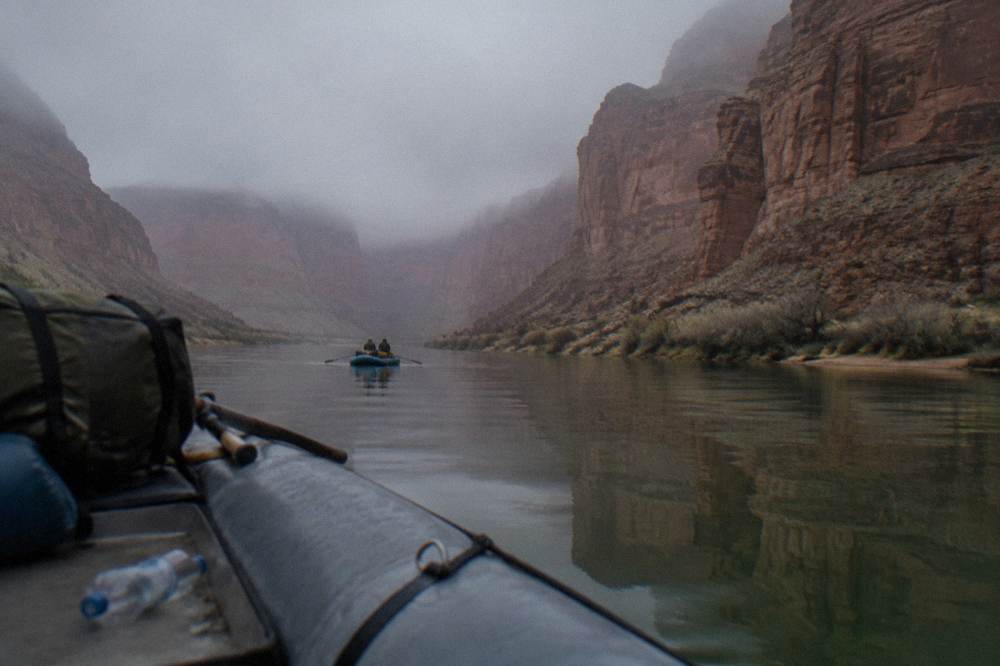 A calm river reflecting canyon walls with a small raft drifting on flat green water
