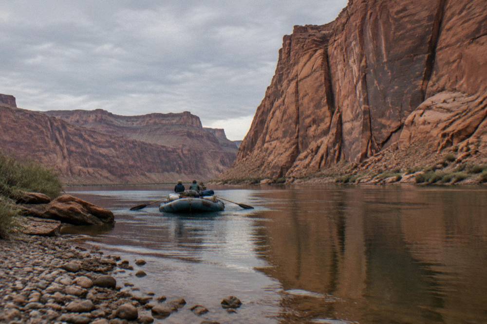 A smooth-water river raft with passengers resting paddles while drifting past red rock cliffs
