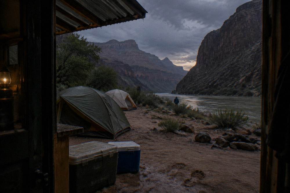 A camping setup on a sandy river beach inside a deep canyon at dusk