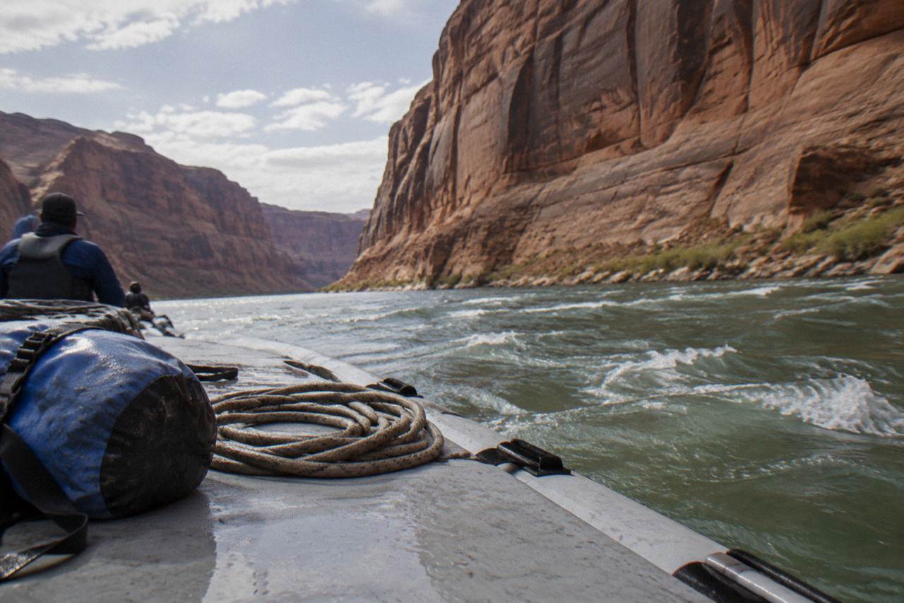 A motorized raft drifting along a calm stretch of the Colorado River beneath tall canyon walls