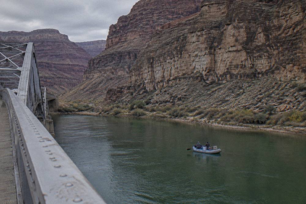 A motorized raft drifting on flat green water beneath steep rock cliffs