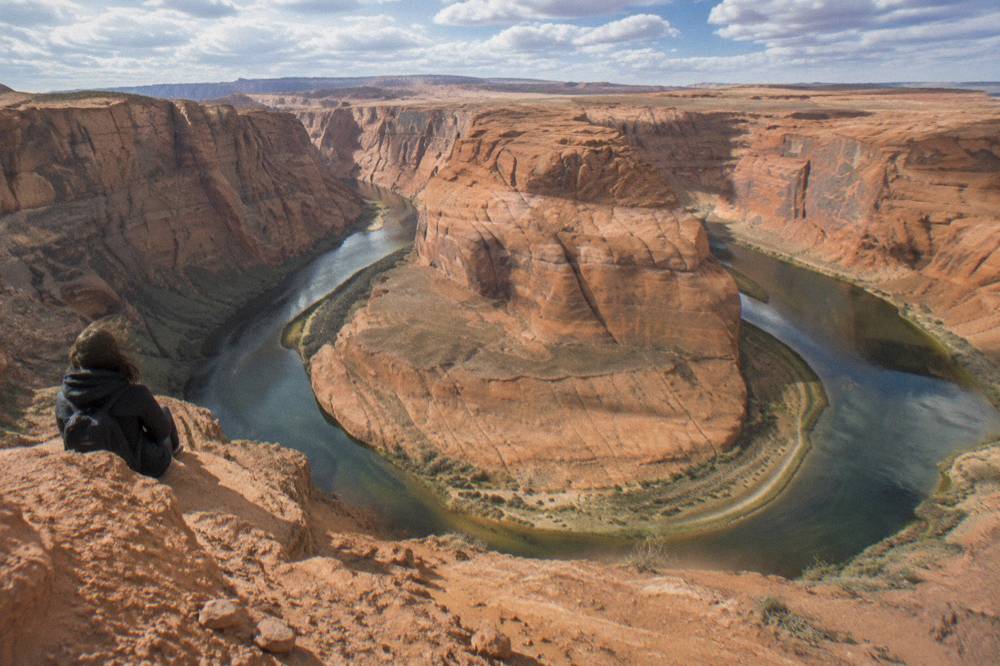A wide river bend curving between orange sandstone cliffs under scattered clouds