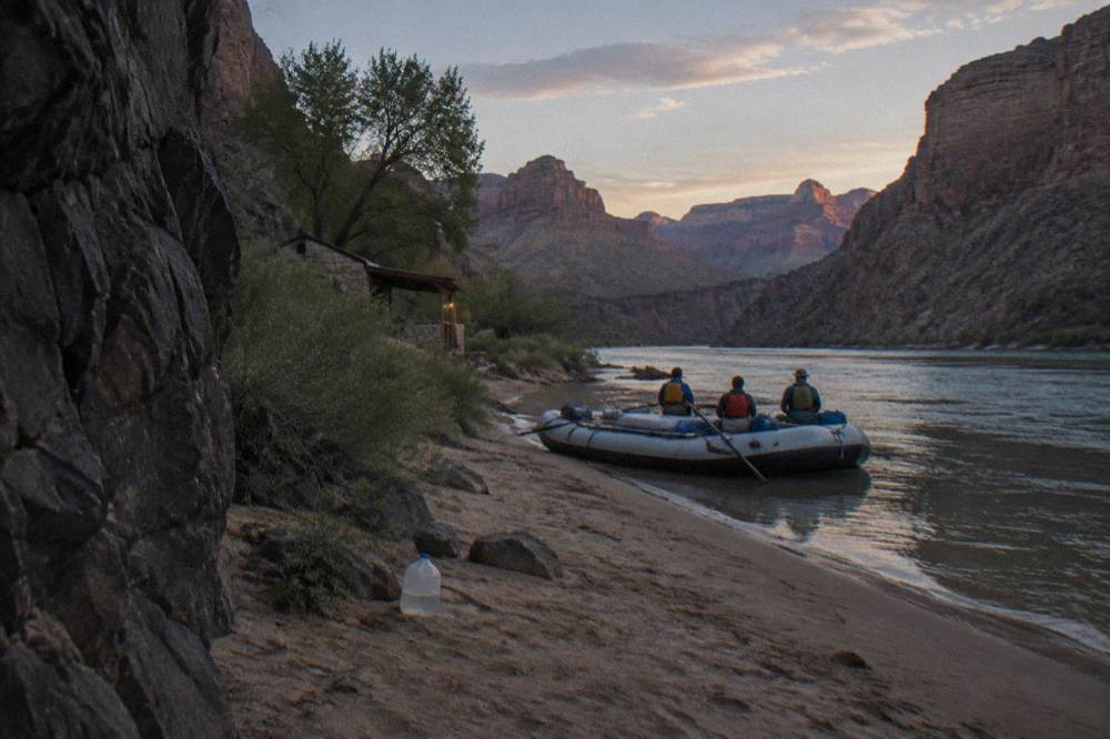 A raft with passengers in life jackets resting beside a sandy river beach in a deep canyon