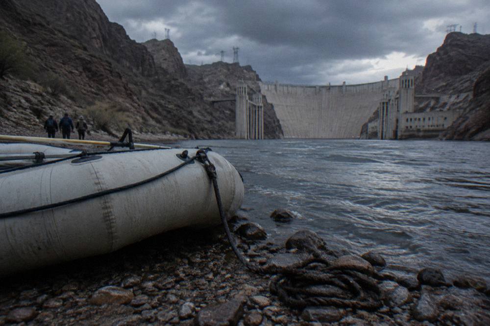 A tour raft at a rocky launch beach beneath the concrete wall of Hoover Dam