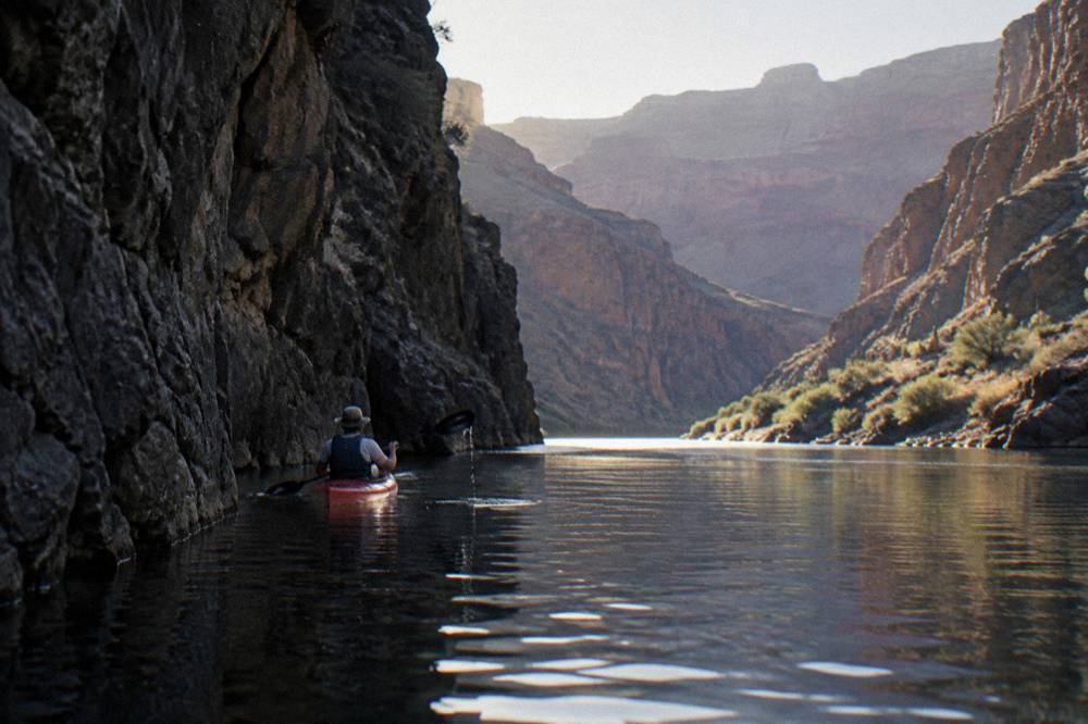 Sunlight on calm river water inside a narrow canyon passage with dark rock walls