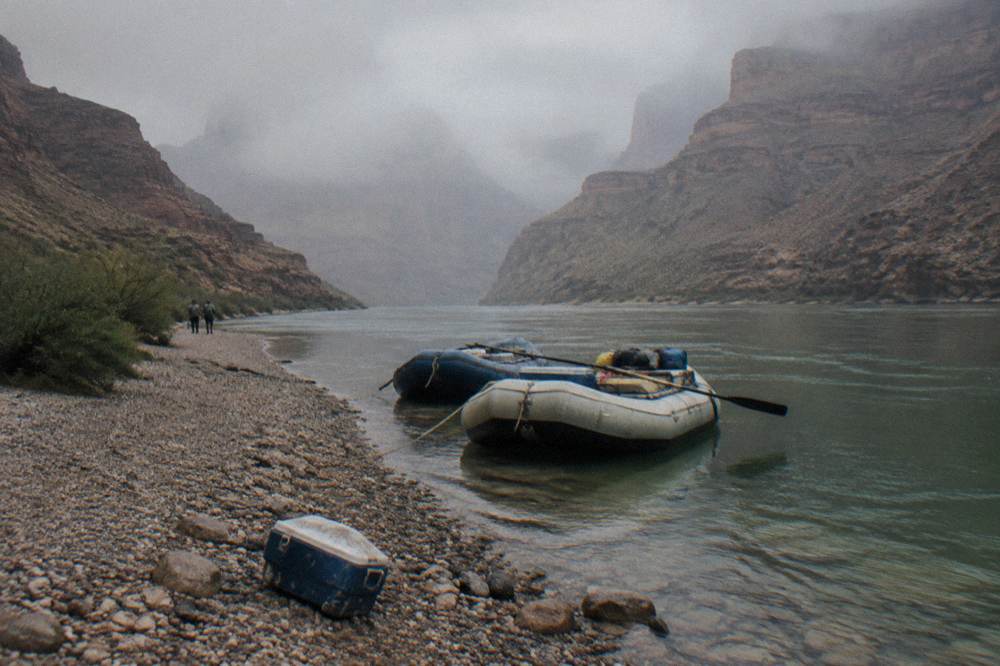A rafts moored at a gravel beach beside calm river water in a canyon