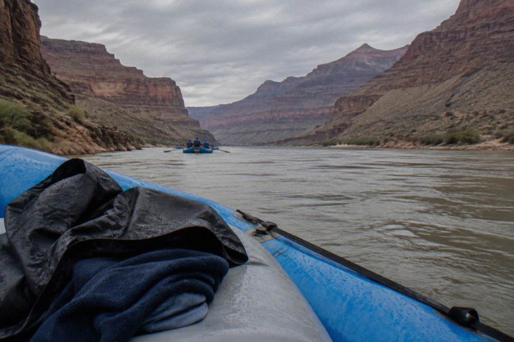 A wind shell and fleece layered over a synthetic shirt on a raft seat