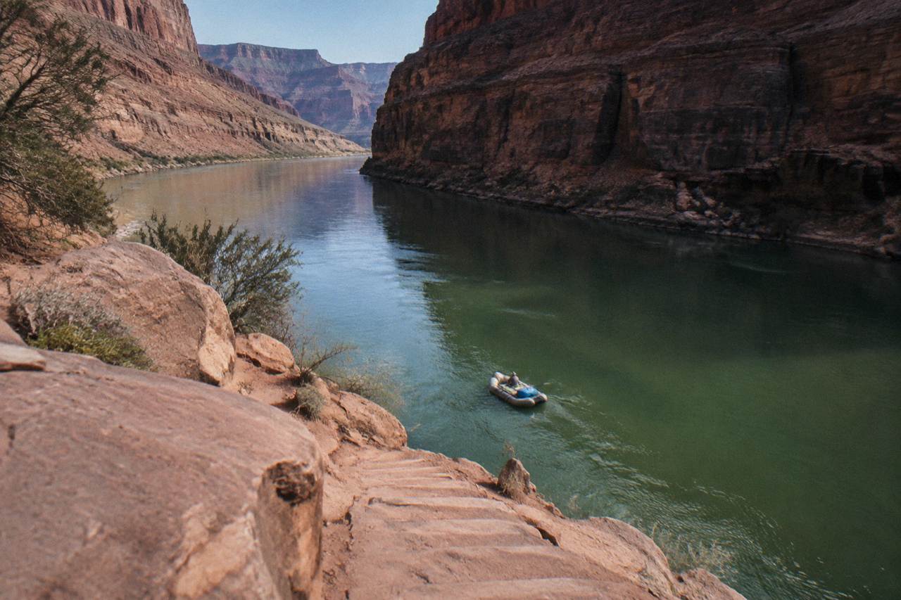 A raft drifting between dark canyon walls above the green Colorado River
