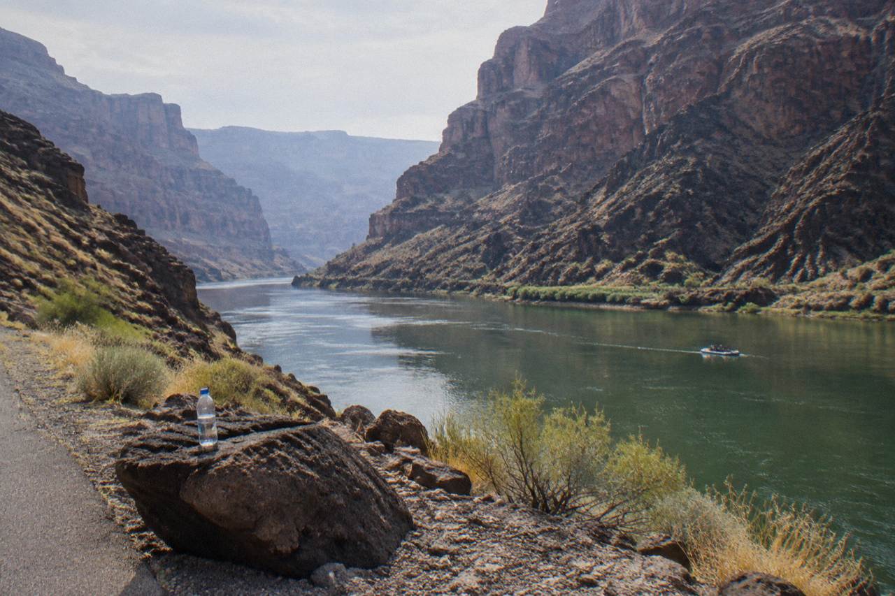 Canyon walls rising above calm green river water with a raft in the distance