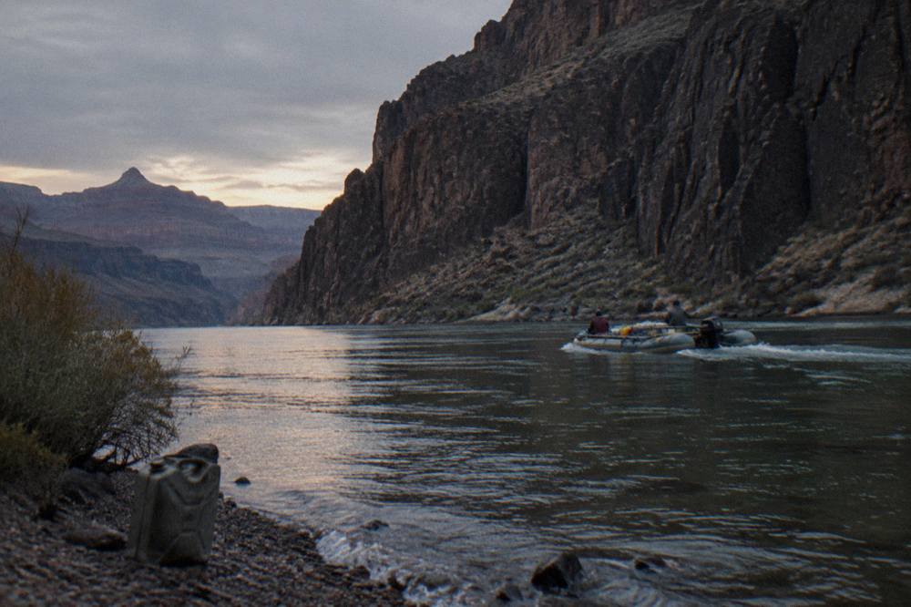 A motorized raft drifting past tall volcanic rock walls along a desert river