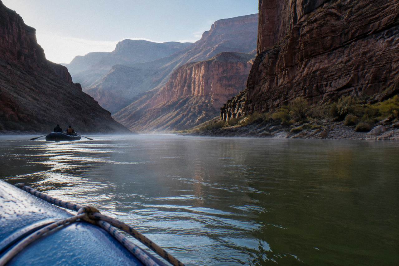 A calm stretch of the Colorado River between dark canyon walls under morning light