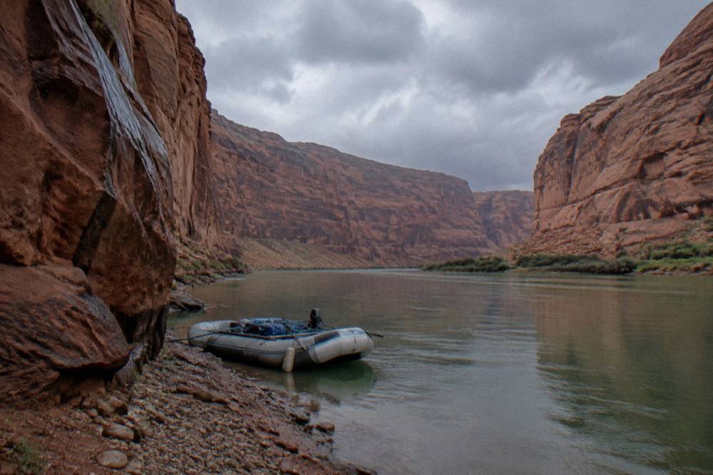 A motorized raft drifting on a calm green river between tall sandstone canyon walls