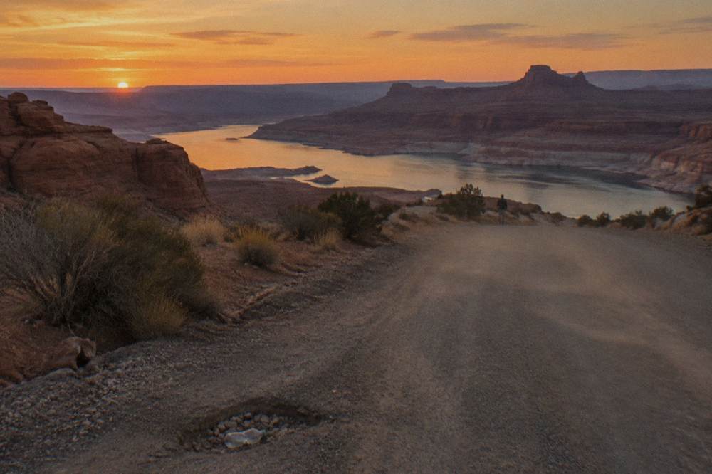 Desert plateau road at dusk with distant canyon formations under a wide orange sky