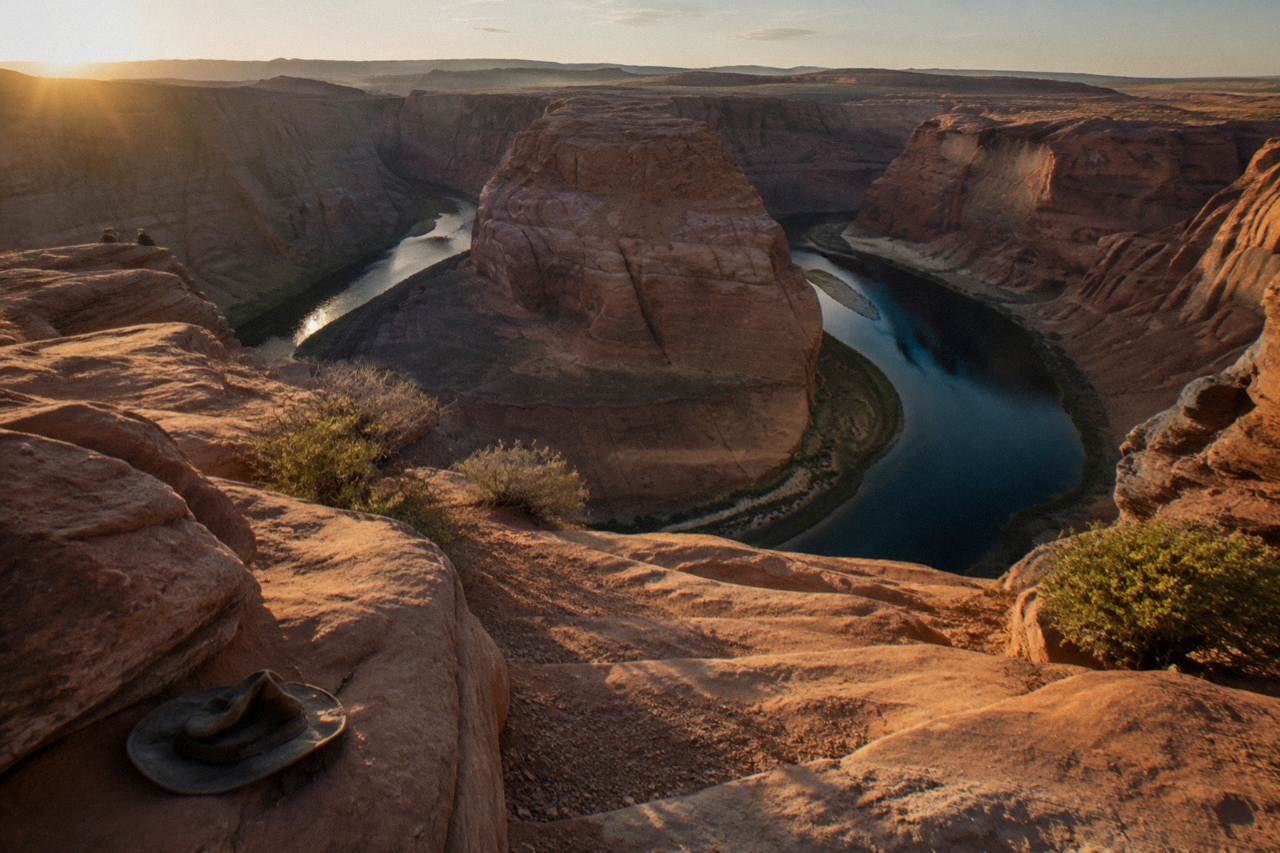 Wide desert view of a horseshoe-shaped river bend below sandstone cliffs at golden hour