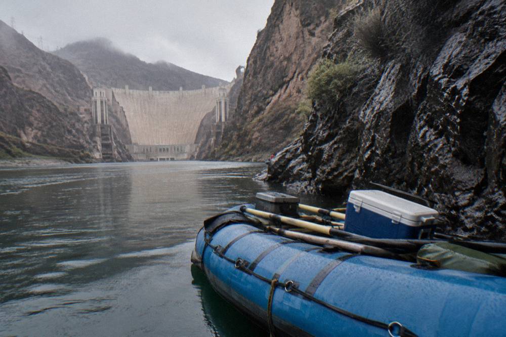 Raft floating on still green water beneath tall volcanic rock cliffs in a desert canyon