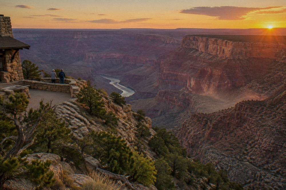 Wide view of layered canyon walls above a calm bend of the Colorado River at sunset