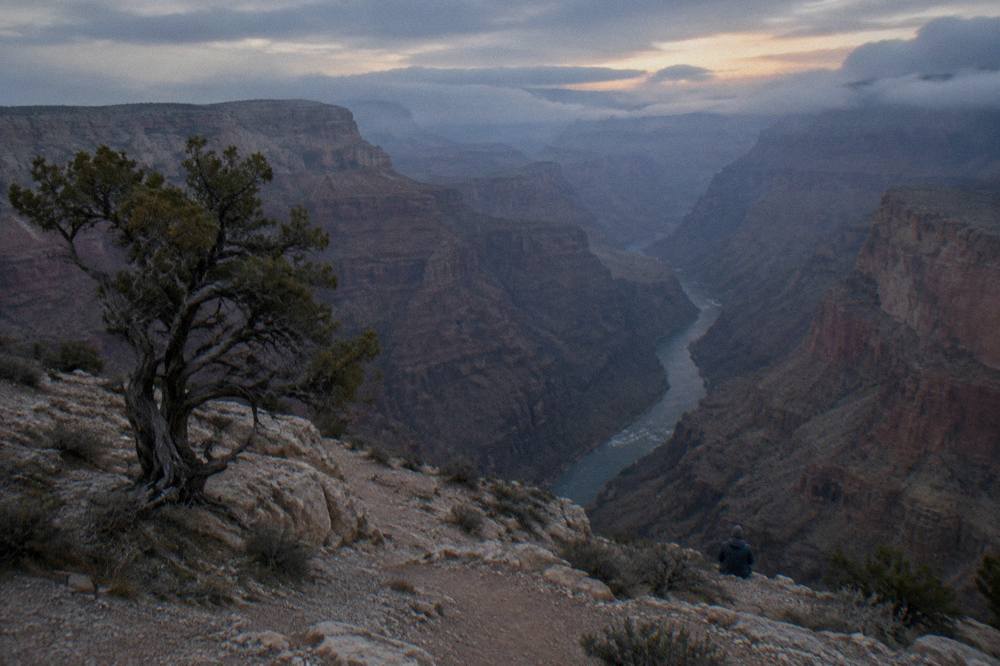 Steep canyon walls dropping toward a narrow band of river at the canyon floor